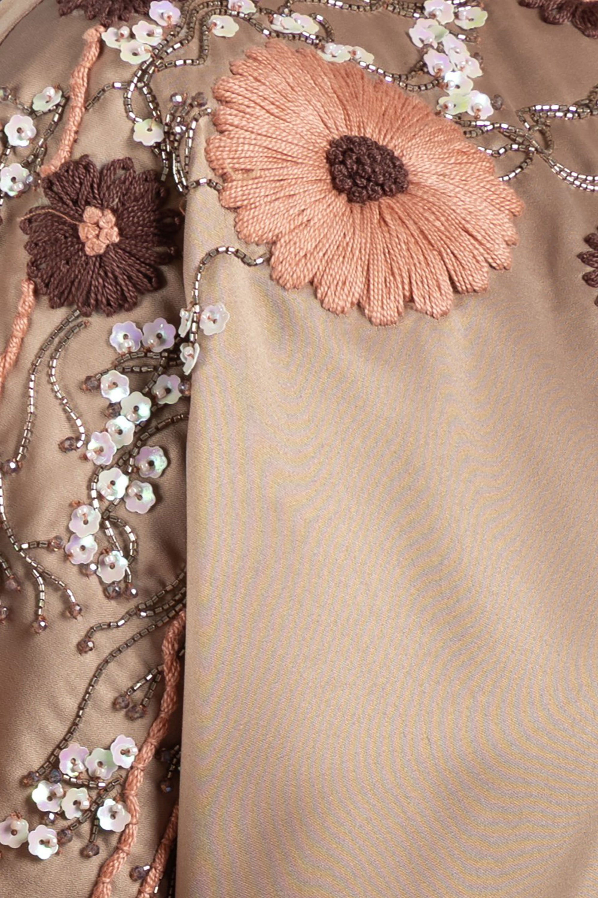 Close-up of embroidered fabric with flowers and sequins on a beige background.