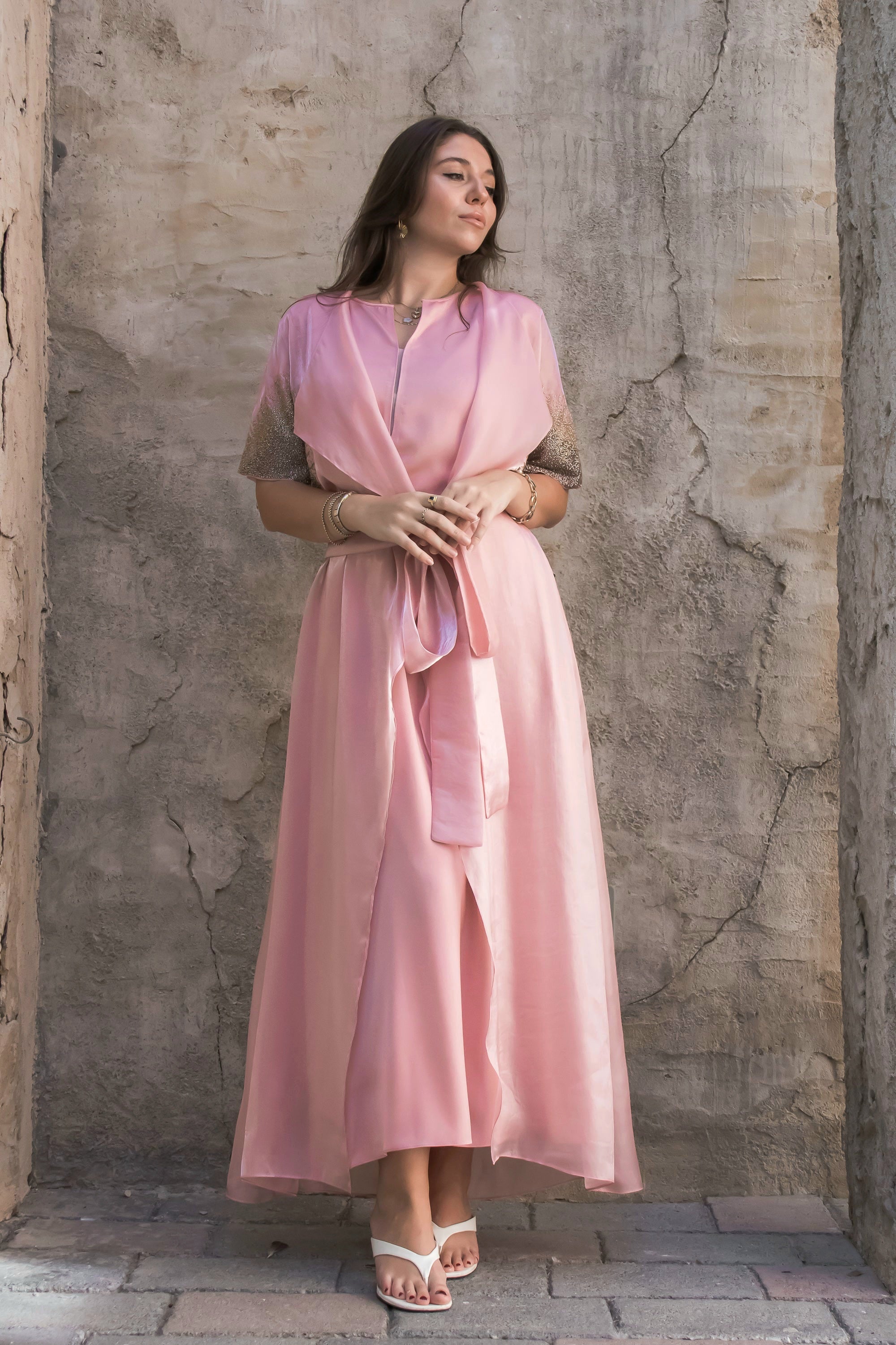 Woman wearing a pink dress standing against a textured stone wall.