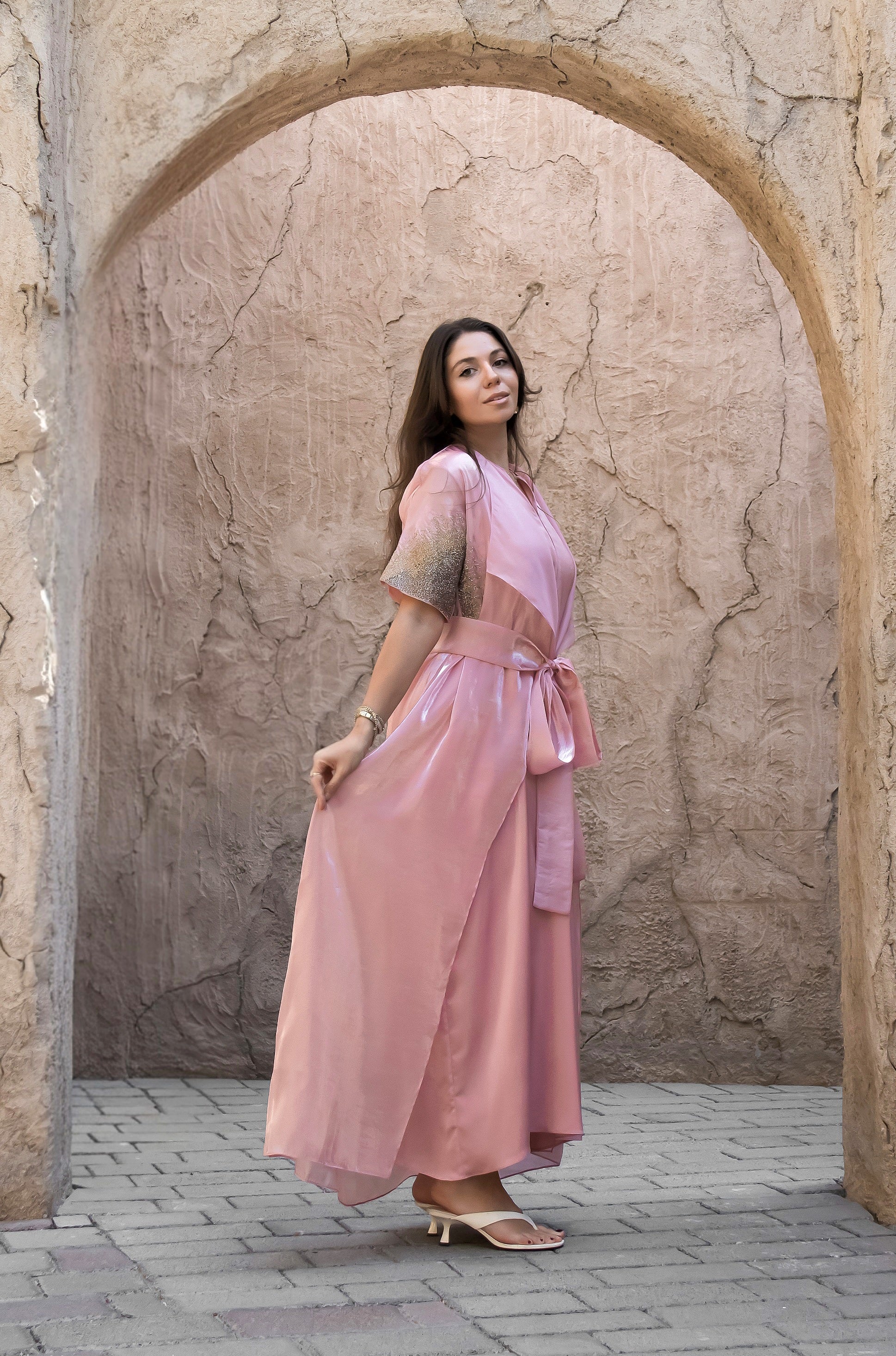 Woman in a pink dress standing in front of a stone archway.
